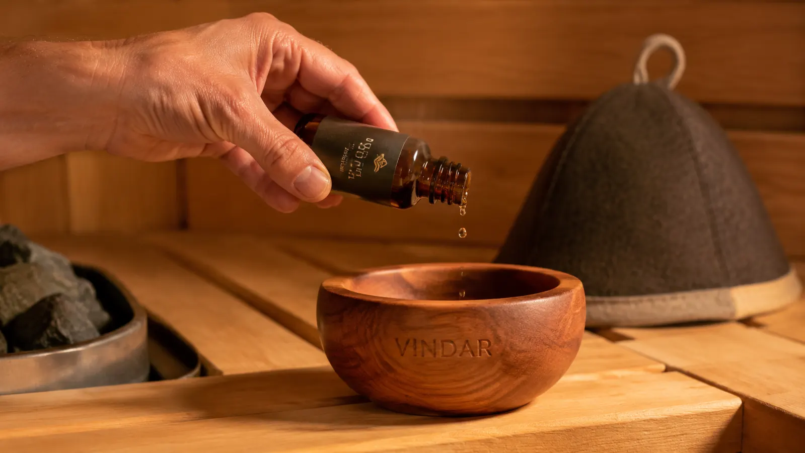Hand using a glass dropper to add a few drops of eucalyptus essential oil into the Vindar cedar bowl before a sauna session