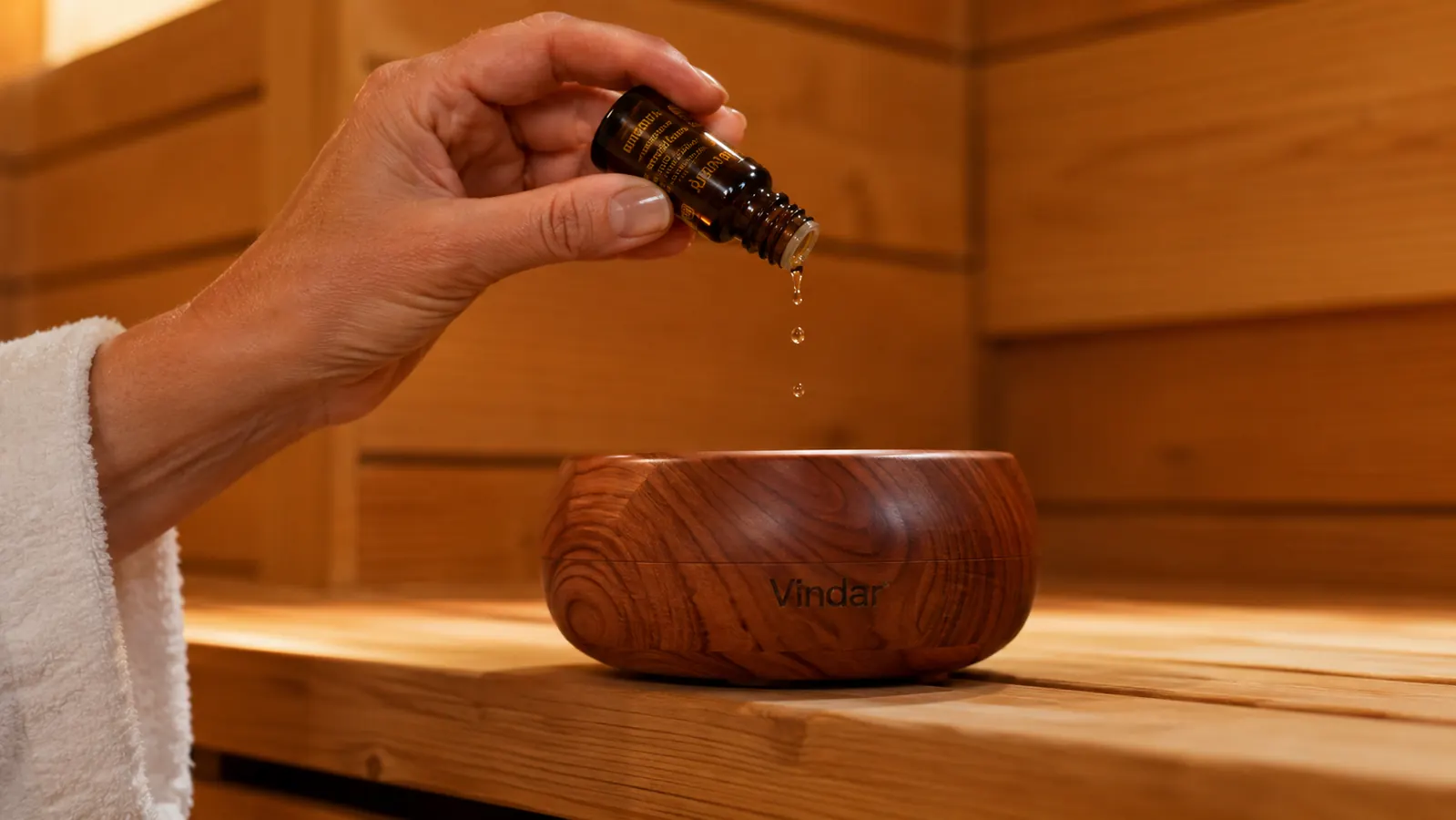 Hand using a glass dropper to add a few drops of eucalyptus oil into the Vindar cedar bowl before a sauna session