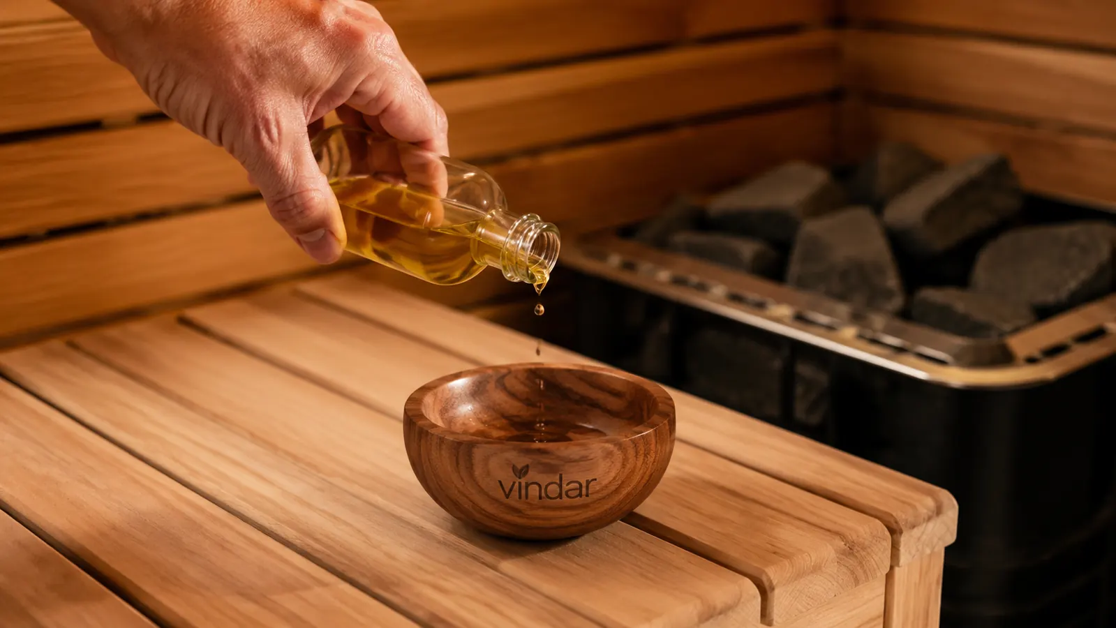 Hand tipping a small bottle of cedarwood oil into the Vindar red cedar aromatherapy bowl on a sauna bench